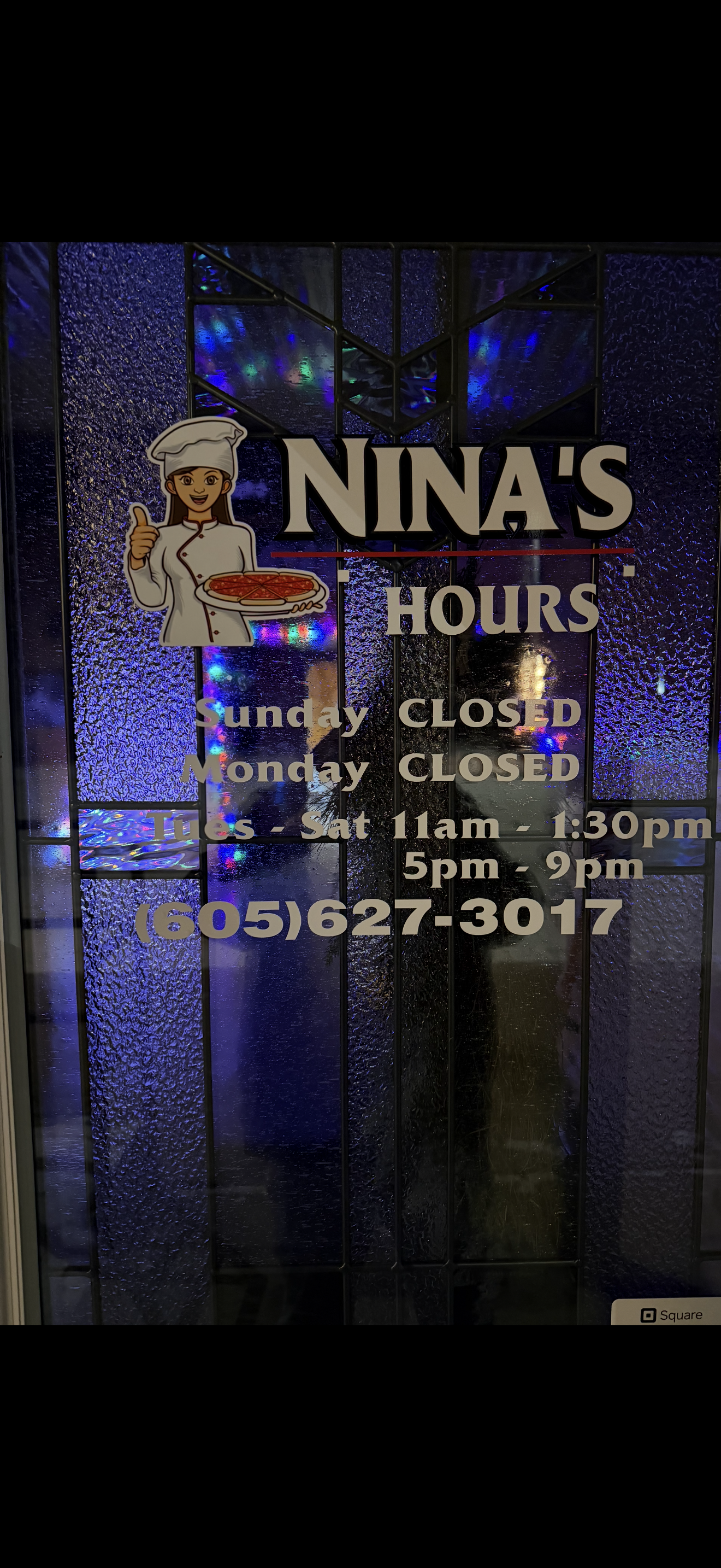 Nina's Pizza Shop hours sign on the front door